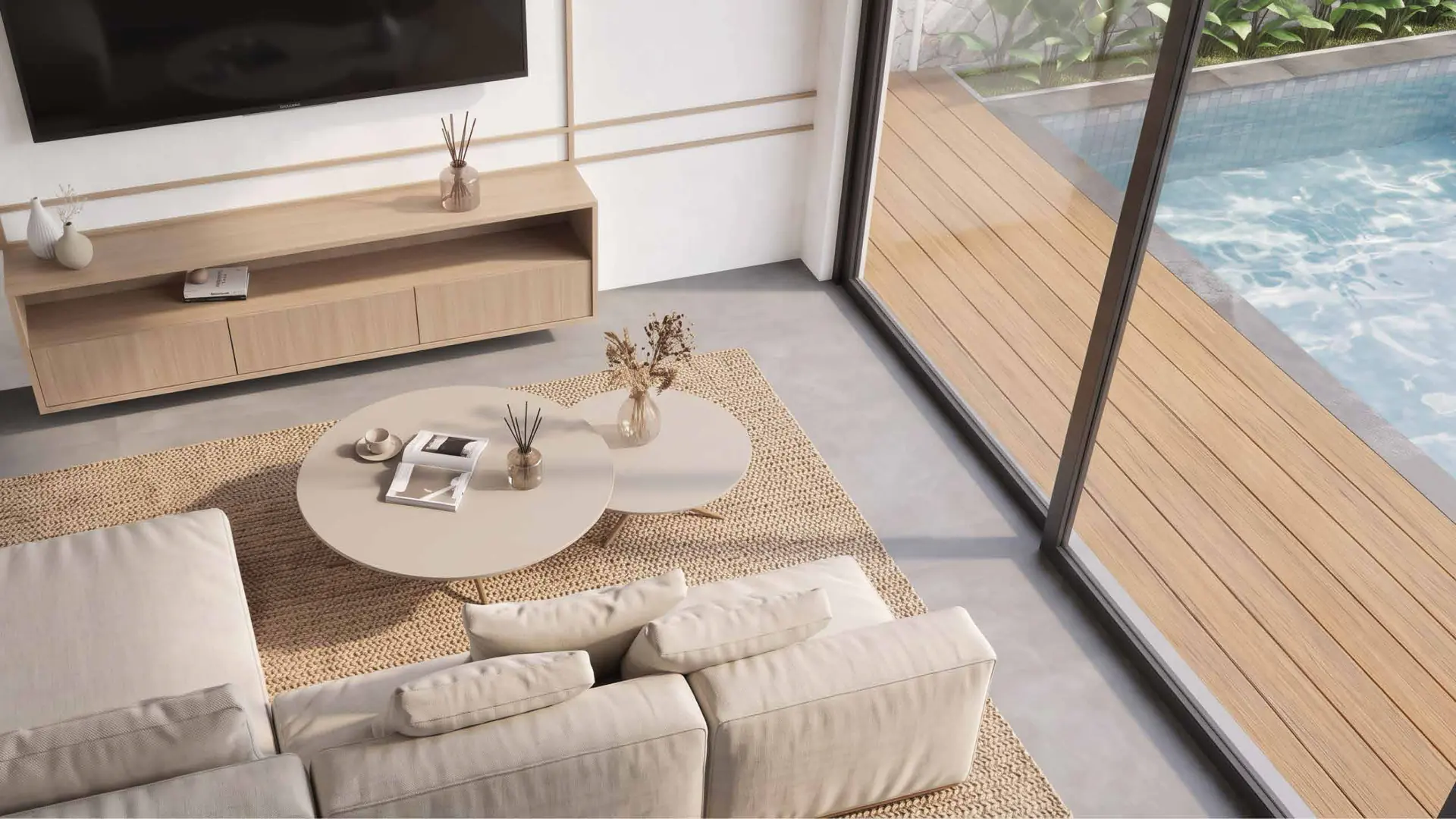 A high view of the living room, its low sofa and jute rug, with the pool deck beyond the glazing.