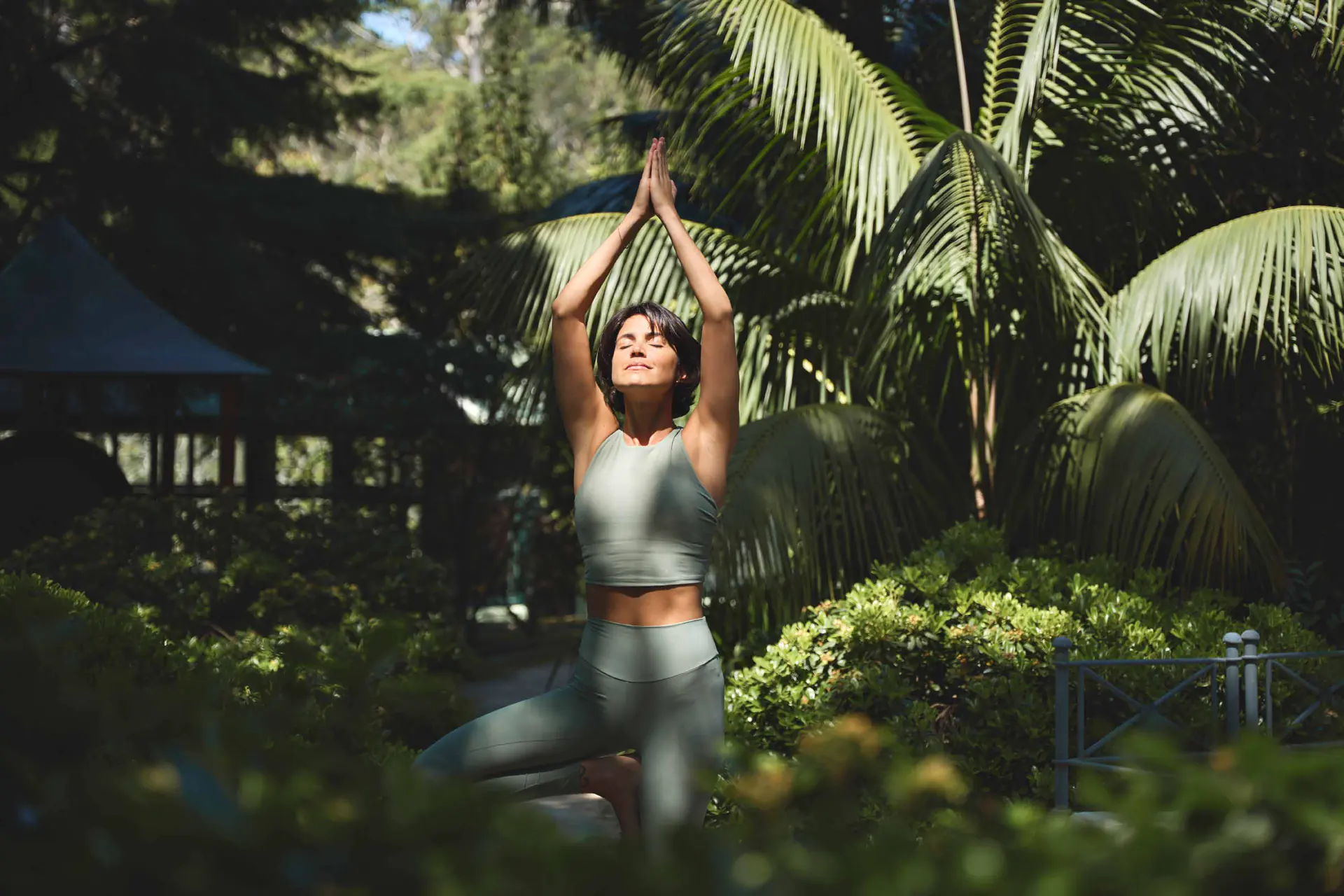 A woman practising yoga in a tropical garden of palms.